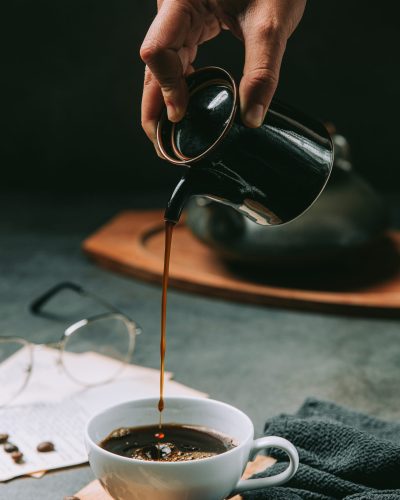 A close-up of a hand pouring coffee water into a coffee cup, international coffee day concept